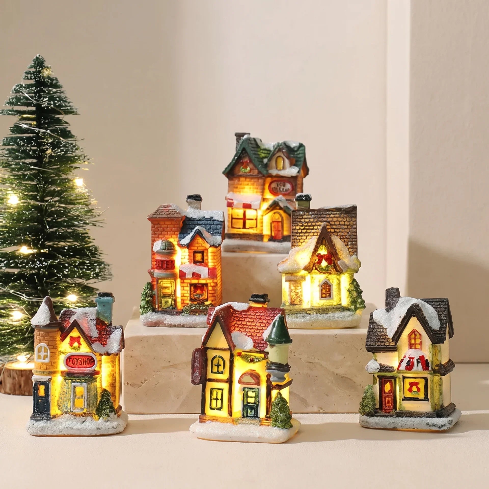 Christmas Village Decoration Set featuring snow-covered miniature houses illuminated by warm LED lights, perfect for tabletop display during the holiday season. 0