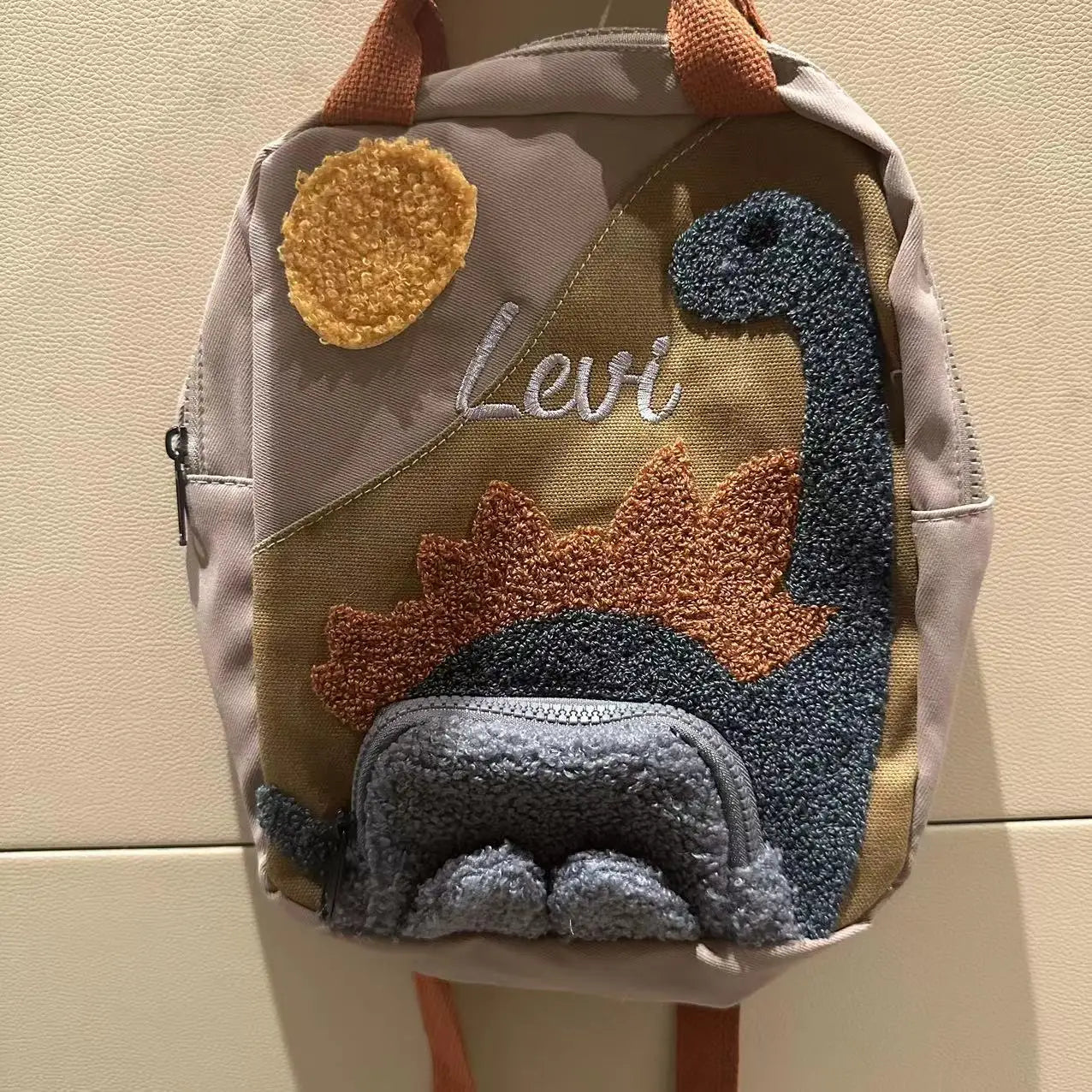 Children's dinosaur backpack featuring customizable embroidery, made from durable canvas with comfortable straps, designed in a fun multi-color pattern. 1
