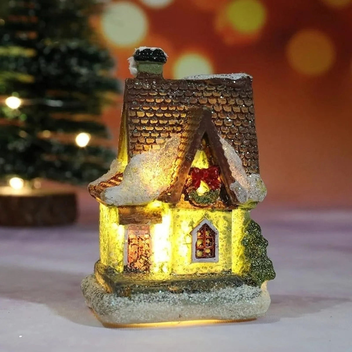 Christmas Village Decoration Set featuring snow-covered miniature houses illuminated by warm LED lights, perfect for tabletop display during the holiday season. 2