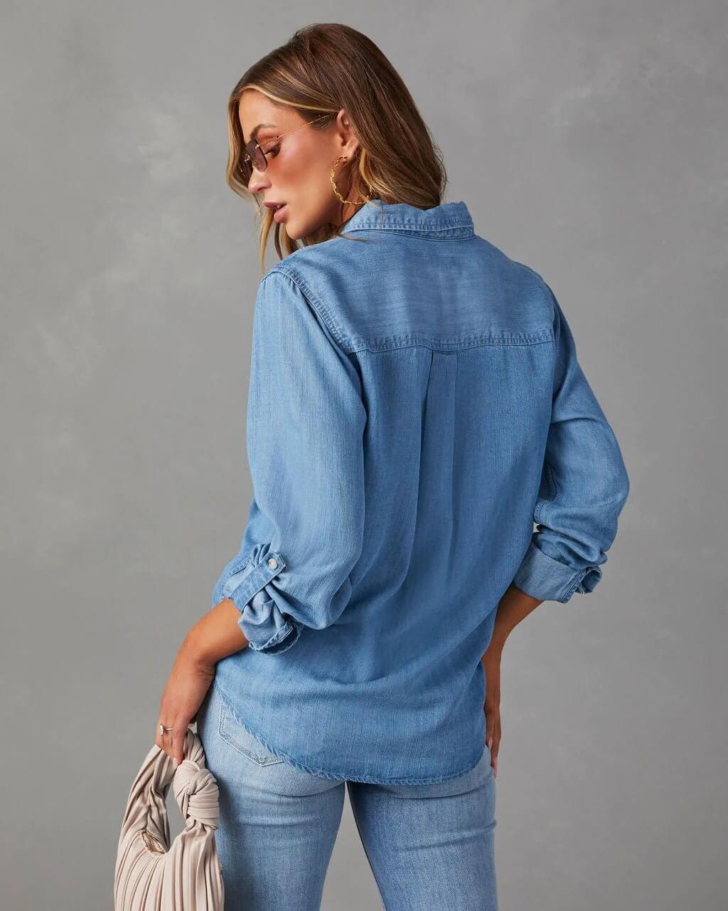 Denim shirt for women featuring a button front, long sleeves, classic collar, and curved hemline. 1